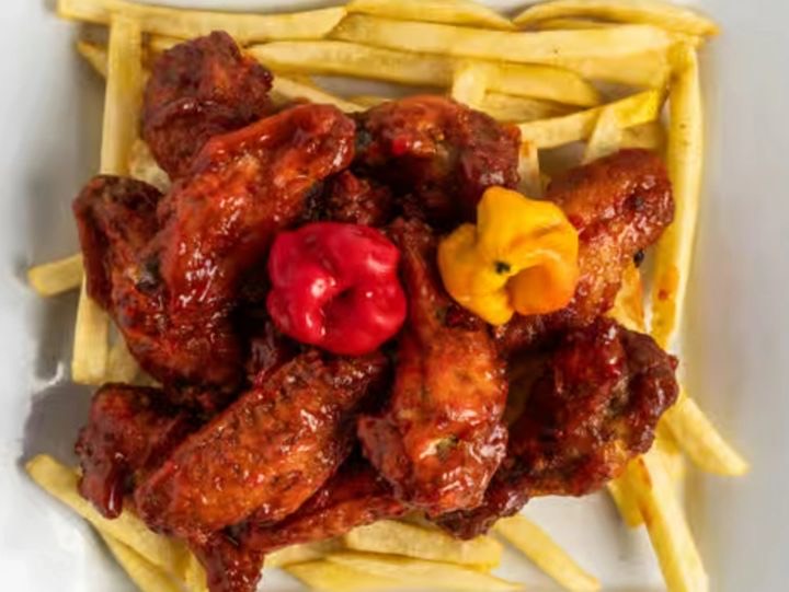 Hot wings in bright red sauce over fries, topped with scotch bonnet peppers